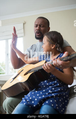 Padre ad insegnare la sua figlia a suonare la chitarra in camera da letto Foto Stock