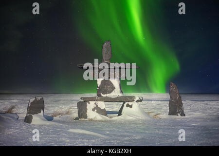 Un simbolo del Nord canadese, una pietra inukshuk siede nella neve con l'aurora boreale in background. significa 'Voi siete sulla strada giusta". Foto Stock