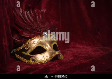 Golden carnevale veneziano maschera con piume rosso visto dal lato su un drappo di velluto rosso teatro tenda Foto Stock