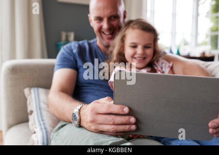 Padre e figlia sit utilizzando un tablet insieme a casa Foto Stock