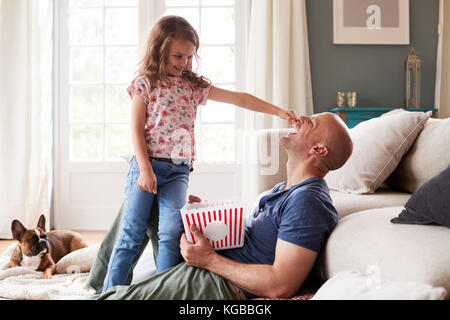 Ragazza sta alimentando il papà di popcorn, guardati da cane a casa Foto Stock