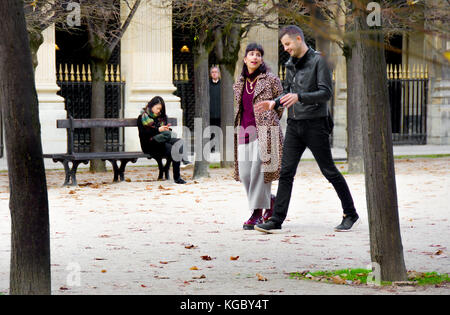 Parigi, Francia. Palais Royal. Autunno, donna relax su un banco, una coppia giovane a piedi (in passato e un spooky man tra gli alberi) Foto Stock