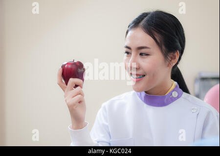 Dentista femmina azienda mela rossa in mano mentre in piedi di fronte ad apparecchiature dentali e dispositivi in clinica. heath care e il concetto di manutenzione Foto Stock