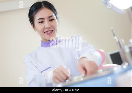 Dentista femmina scegliere alcuni strumenti dalla barra in metallo in clinica di cura dentale e sano concetto di manutenzione Foto Stock