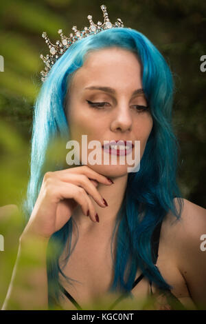 Donna con capelli blu che indossa una corona tra foglie Foto Stock