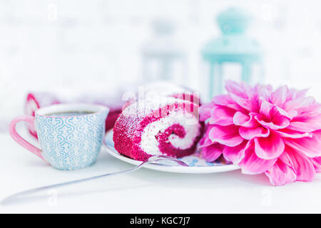 Una torta rossa del velluto rotolo tagliato con tazza di caffè o tè e fiori. sfondo bianco. Foto Stock