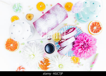 Una torta rossa del velluto rotolo tagliato con tazza di caffè fiori e dolci secchi Arance. vista dall'alto. sfondo bianco. Foto Stock
