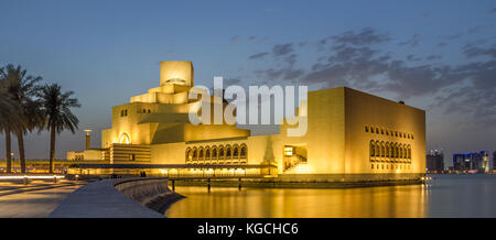 Il Museo di Arte Islamica, Doha, Qatar di notte vista esterna con la riflessione della luce nel Golfo Arabico con alberi e grattacieli in background. Foto Stock