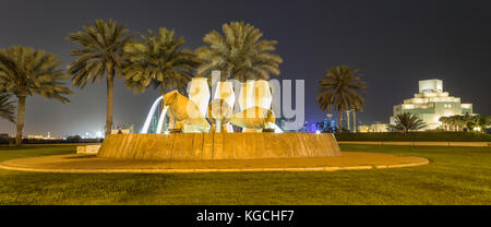 Doha, skyline del Qatar di notte che mostra il Museo d'arte islamica, fontana del vaso d'acqua, alberi e grattacieli sullo sfondo. Foto Stock