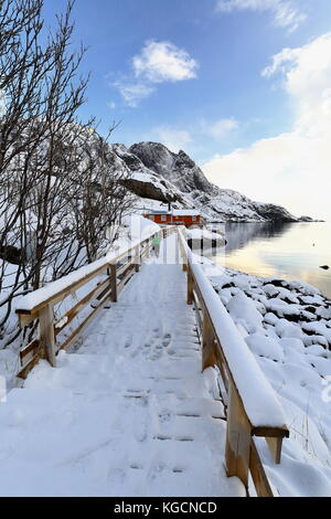 Coperta di neve plank passerella che conduce al rosso rorbuer-legno tradizionali capanne di pesca ora per uso turistico nella zona di vika alla s.di pesca nusfjord vi Foto Stock