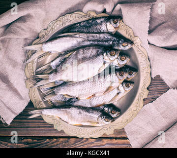 Asciugato il pesce salato di ram in una piastra di ferro su un di legno marrone, sfondo vista superiore Foto Stock