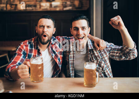 Tre uomini con birra gioire la vittoria della loro squadra preferita nel pub Foto Stock