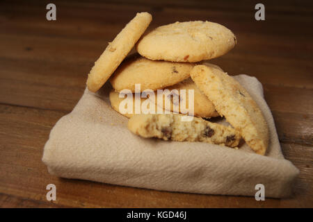 Selezione di choc chip di frutta e biscotti, su un tovagliolo su una tavola di legno Foto Stock