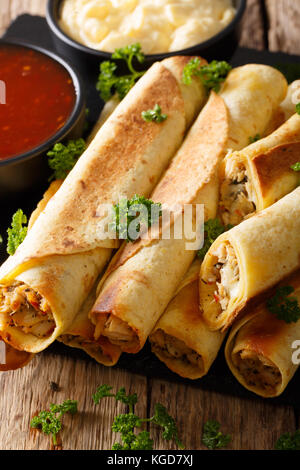 Taquitos messicano con pollo e ripieno di formaggio di close-up e le salse sul piano verticale. Foto Stock