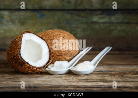 Tutto fresco tagliato a metà noci di cocco con scaglie di noce di cocco e trita in cucchiai su sfondo di legno con spazio di copia Foto Stock