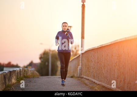 Giovane donna sportiva jogging sul ponte la mattina. esecuzione di ragazza fitness in sportswear immagine esterna con spazio di copia Foto Stock