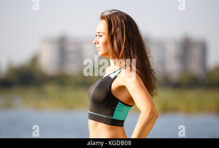 Ritratto di giovane donna sportiva riposo dopo un po' di jogging nel parco vicino lago. ritratto della ragazza di atletica nella parte superiore nera dopo allenamento fitness Foto Stock