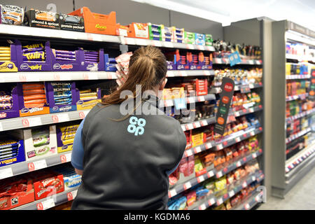 Ripiano impilaggio in co-operativa negozio alimentare, vista posteriore di un membro dello staff di cioccolato di impilamento su un ripiano. Foto Stock
