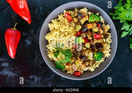 Luce alimentari sane piatto vegano: cuscus e verdure (zucchine, melanzane, carote, peperoni, cipolle, prezzemolo) su uno sfondo nero. top Foto Stock