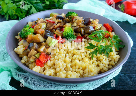 Luce alimentari sane piatto vegano: cuscus e verdure (zucchine, melanzane, carote, peperoni, cipolle, prezzemolo) su uno sfondo nero. Foto Stock
