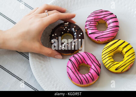 Mani femminili della scatola di contenimento con ciambelle colorate in blu sullo sfondo di legno Foto Stock