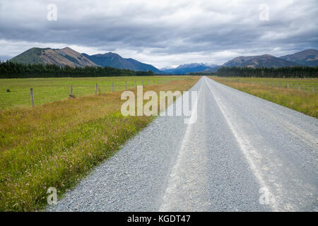 Dritto su strada di ghiaia attraverso il pascolo in Nuova Zelanda con le montagne sullo sfondo Foto Stock