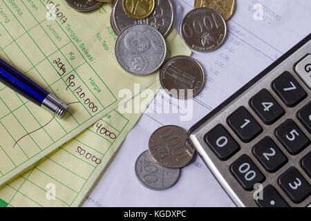 Vista dall'alto/calcolo della ricevuta di pagamento con rupia indonesiana e monete in dollari di Singapore, calcolatrice e fatture scritte a mano Foto Stock