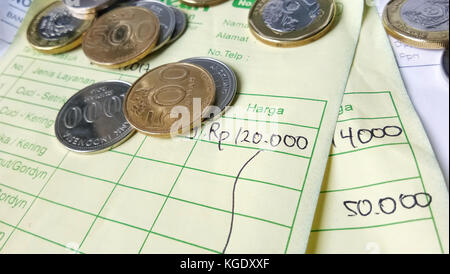 Calcolo della ricevuta di pagamento con rupia indonesiana, monete in dollari di Singapore e fatture scritte a mano Foto Stock
