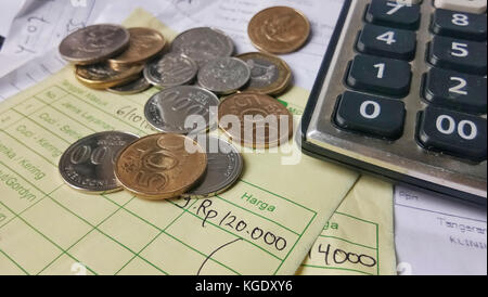 Calcolo della ricevuta di pagamento con vista dall'alto/piatto, con monete in rupia indonesiana e dollari di Singapore, calcolatrice e fatture scritte a mano Foto Stock