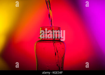 Ancora la vita di una bottiglia di acqua essendo riempito con acqua con un multi colore di sfondo Foto Stock