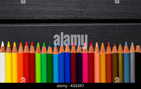 Colorate matite colorate su di un legno nero, sfondo allineati su un gradiente arcobaleno Foto Stock