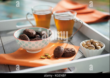 Rustico con biscotti al cioccolato e noci in tazza di ceramica, servito sul vassoio in legno con due tazze di tè e un bicchiere di fresco di pistacchi Foto Stock