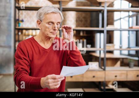 Grave uomo anziano tenendo i suoi occhiali Foto Stock