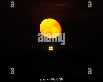 Sheerness, Kent, Regno Unito. 6 Nov, 2017. Regno Unito: Meteo sorgere della luna sopra l'estuario del Tamigi. La luna è apparso un cupo colore rosso come è salito sopra l'orizzonte. Il cluster di luci sono da una nave ancorata in estuario. Credito: James Bell/Alamy Live News Foto Stock