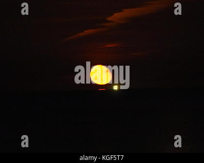 Sheerness, Kent, Regno Unito. 6 Nov, 2017. Regno Unito: Meteo sorgere della luna sopra l'estuario del Tamigi. La luna è apparso un cupo colore rosso come è salito sopra l'orizzonte. Il cluster di luci sono da una nave ancorata in estuario. Credito: James Bell/Alamy Live News Foto Stock