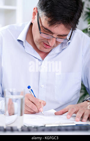 Un uomo d'affari concentrato di alto livello che scrive in ufficio Foto Stock