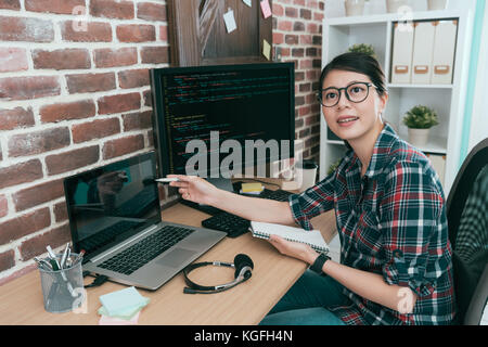 Giovane programmatore sorridente manager laptop rivolta verso il piano di sviluppo di parlare del documento con un collega e riuniti insieme per discutere la progettazione dei dati. Foto Stock