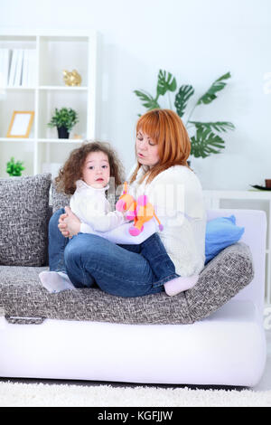 Giovane madre sdraiato sul divano e giocare con la sua felice amorevole figlia piccola - indoor Foto Stock