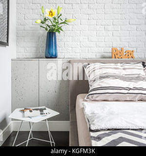 Luminose lenzuola sul letto king-size contro un muro di mattoni con dipinti  in semplice stanza da letto con lampade Foto stock - Alamy