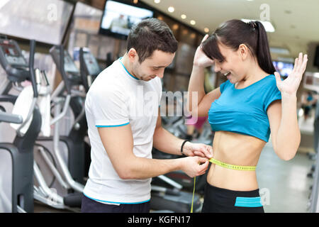 Donna con personal trainer in palestra sorpreso con risultati Foto Stock