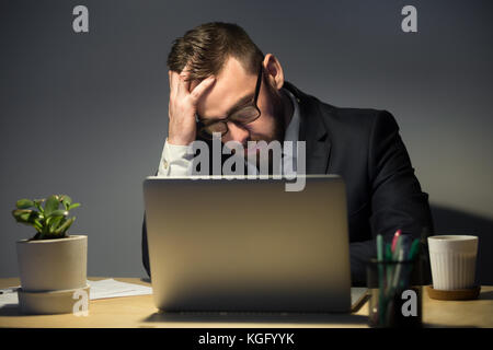 Troppo concetto di lavoro. Uomo turbato in occhiali che legge sul recente problema del computer portatile, profondamente in pensieri sulla migliore linea di azione. Mano su Foto Stock