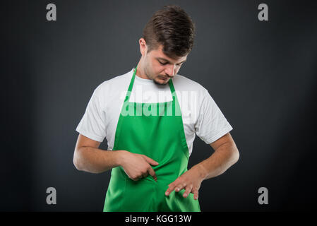 Ritratto supermercato datore di lavoro cercando nel suo grembiule pocket su sfondo nero Foto Stock