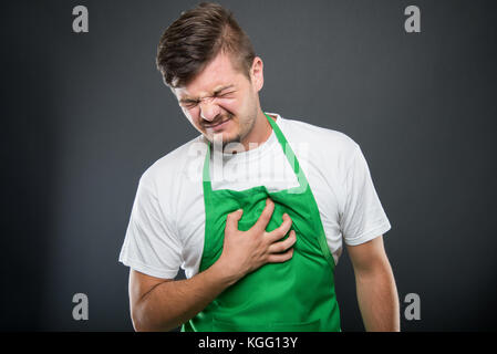 Ritratto di supermercato datore di lavoro tenendo petto come nel dolore su sfondo nero Foto Stock