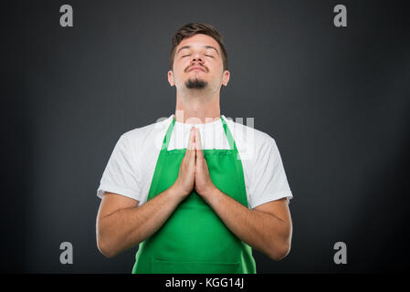 Ritratto supermercato datore di lavoro in piedi in posizione di preghiera come sperando concetto su sfondo nero Foto Stock