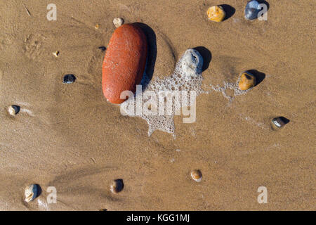 Ciottoli e pietre di rendere attraenti modelli nella sabbia sulla spiaggia Seaham come la marea si ritira, County Durham, Regno Unito Foto Stock