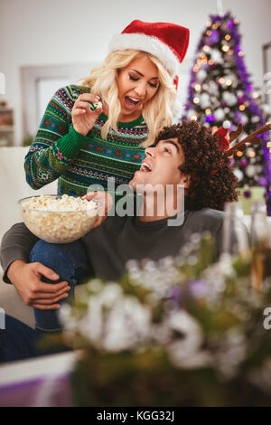 Amare giovane in accogliente maglioni caldi su un Natale Capodanno, sorridente e divertirsi con ogni altro mangiare popcorn. messa a fuoco selettiva. Foto Stock