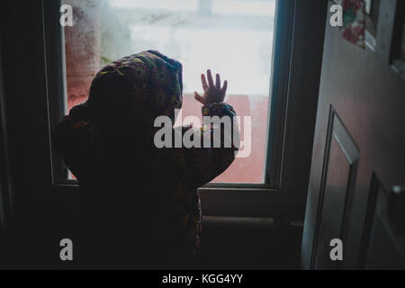 Una bambina guarda fuori una finestra a basse temperature Foto Stock