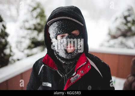 Bambino che indossa una maschera da sci coperta di neve Foto Stock