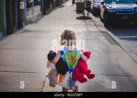 Una bambina cammina verso il basso un marciapiede con una manciata di animali imbalsamati Foto Stock