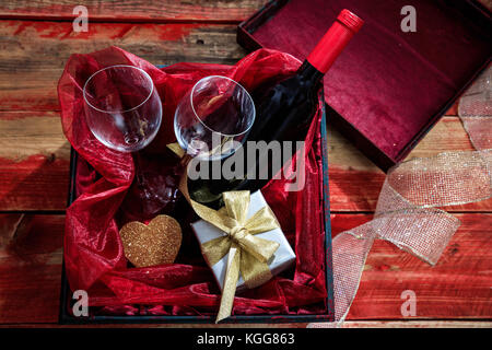 Il giorno di san valentino del concetto. rosso Bottiglia di vino, bicchieri e un dono in un riquadro di sfondo di legno Foto Stock